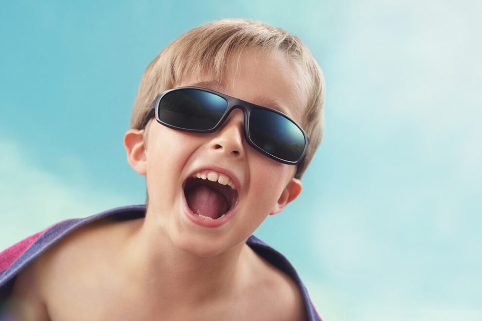 Image a child with happy expression, beach towel and sun glasses.